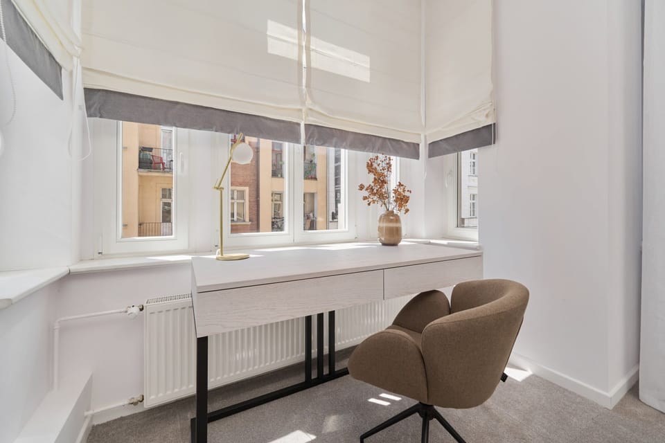 A stylish and minimal workspace with a wooden desk, a chair, and a view out of a large window, offering a bright ambiance.