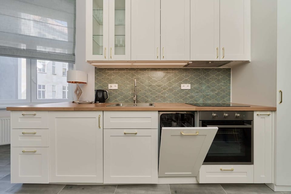 A modern kitchen with sleek light cabinetry, stainless steel appliances, and a tiled backsplash in neutral tones.
