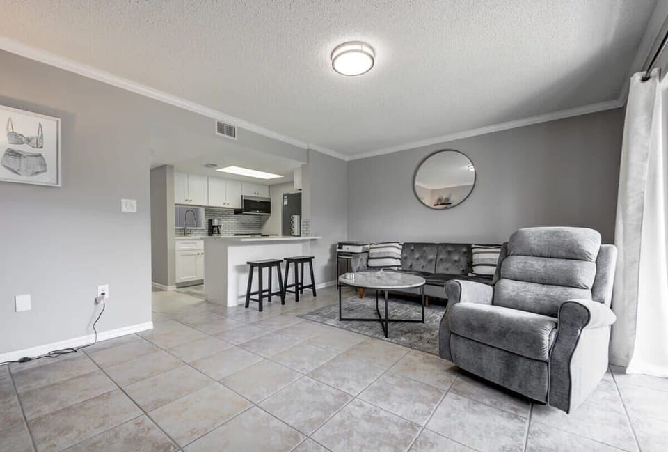 Modern living area with a gray recliner, tufted sofa, and open kitchen with breakfast bar.