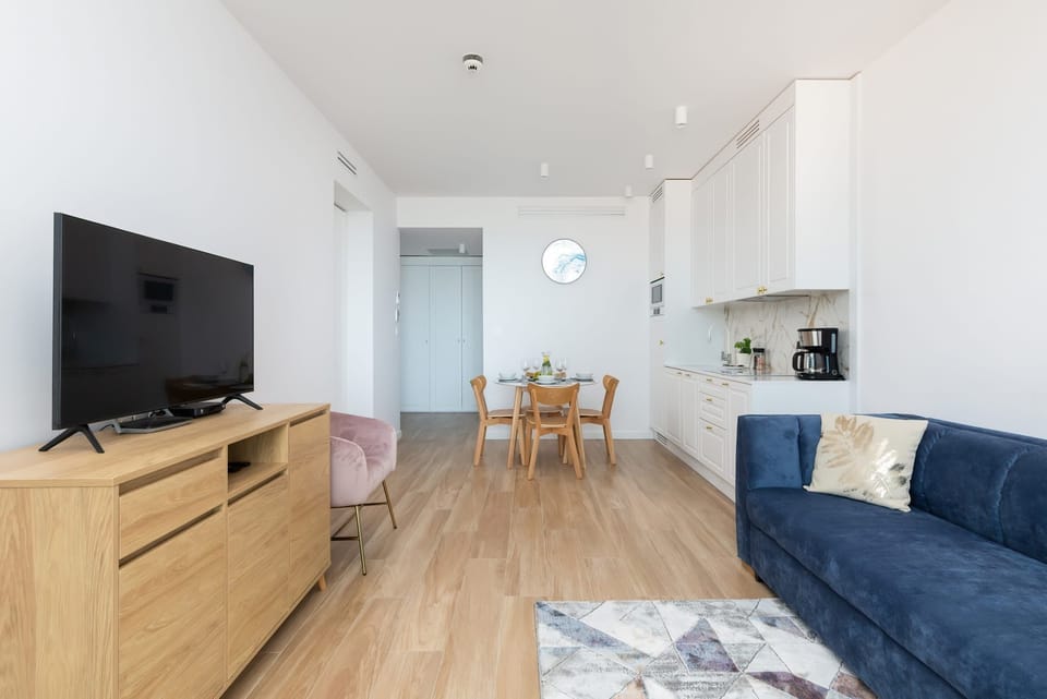 A spacious living room with large windows, a blue sofa, a pink armchair, and a wooden TV stand.