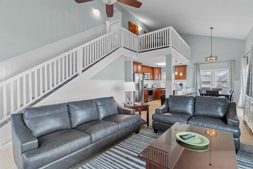 Bright living room with vaulted ceilings, leather seating, coastal art, and windows that bring in natural light and beautiful ocean views.