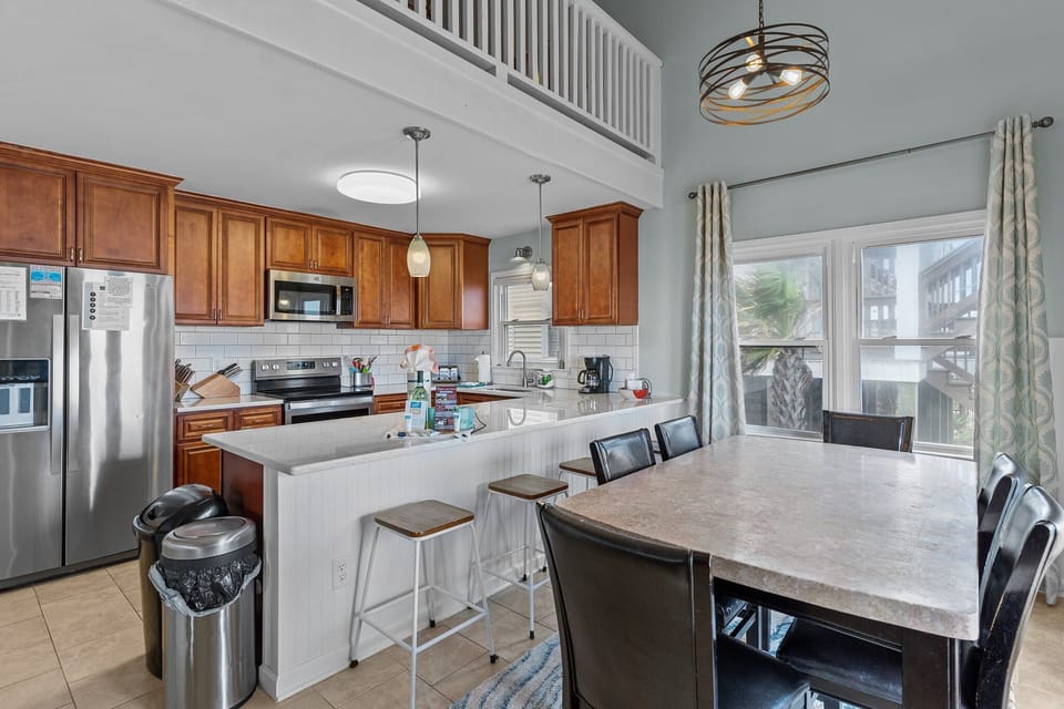 Kitchen with warm wood cabinets, white quartz bar seating, stainless appliances, subway tile backsplash, pendant lights, and coffee station.