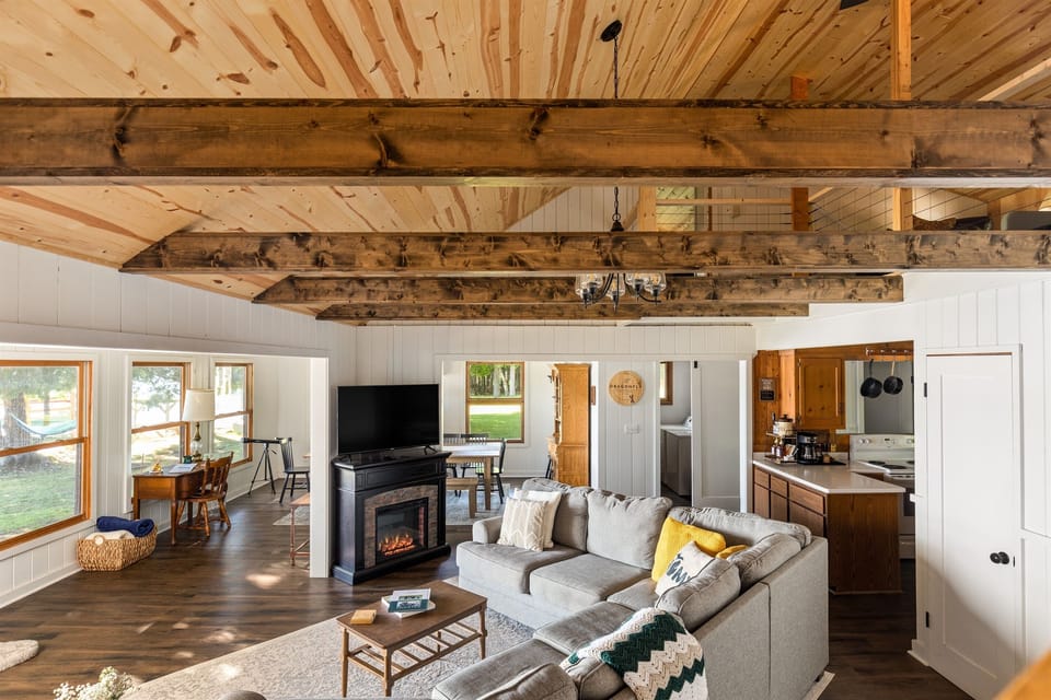 Living room with sectional, exposed beams and open floor plan - connecting to the dining room and kitchen with views of Intermediate Lake right in the backyard.