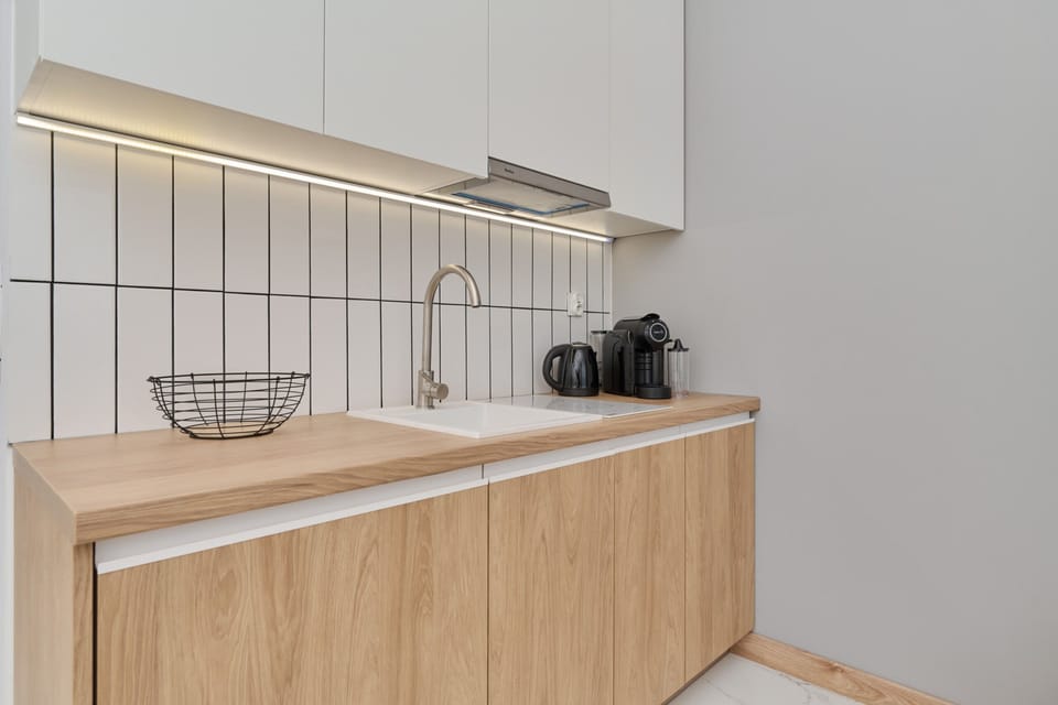 A compact yet fully equipped kitchenette with white and wooden cabinetry, offering a practical and stylish design.

