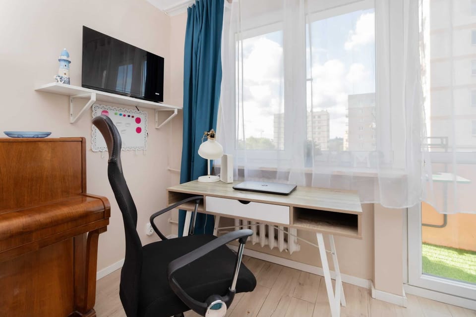 Another angle of the living area with a wall-mounted TV, a small wooden cabinet, and elegant sheer curtains.


