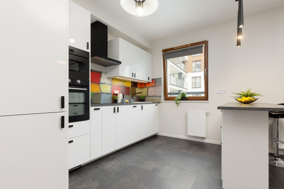 A fully equipped kitchen with sleek white cabinetry, colorful backsplash, and ample counter space for cooking convenience.

