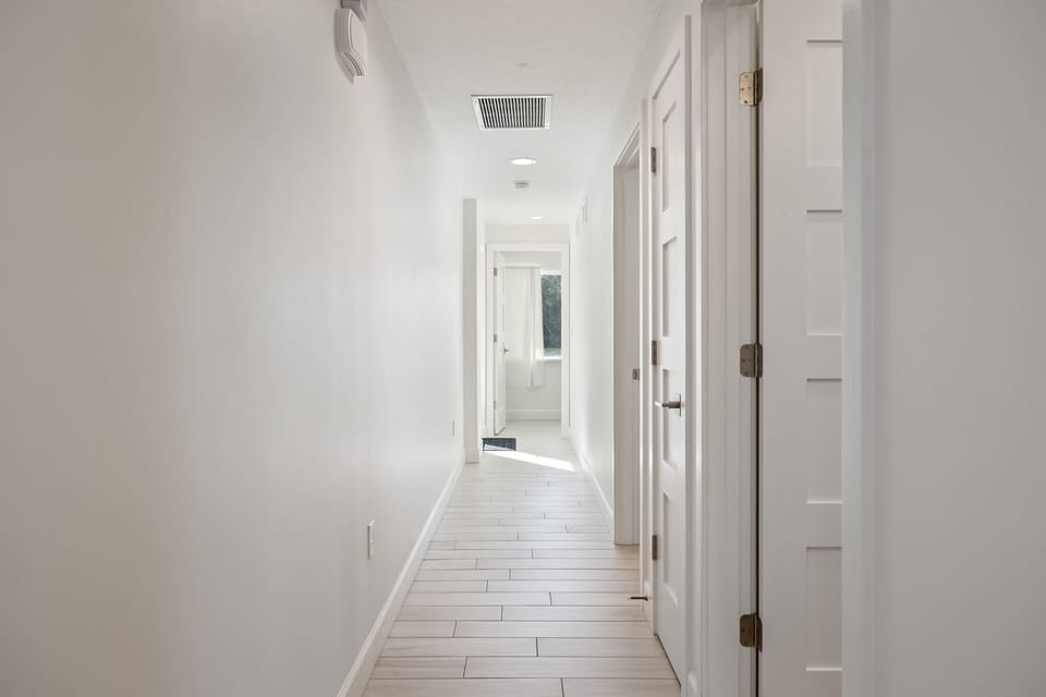 Bright hallway with white walls and tile flooring leading to natural light