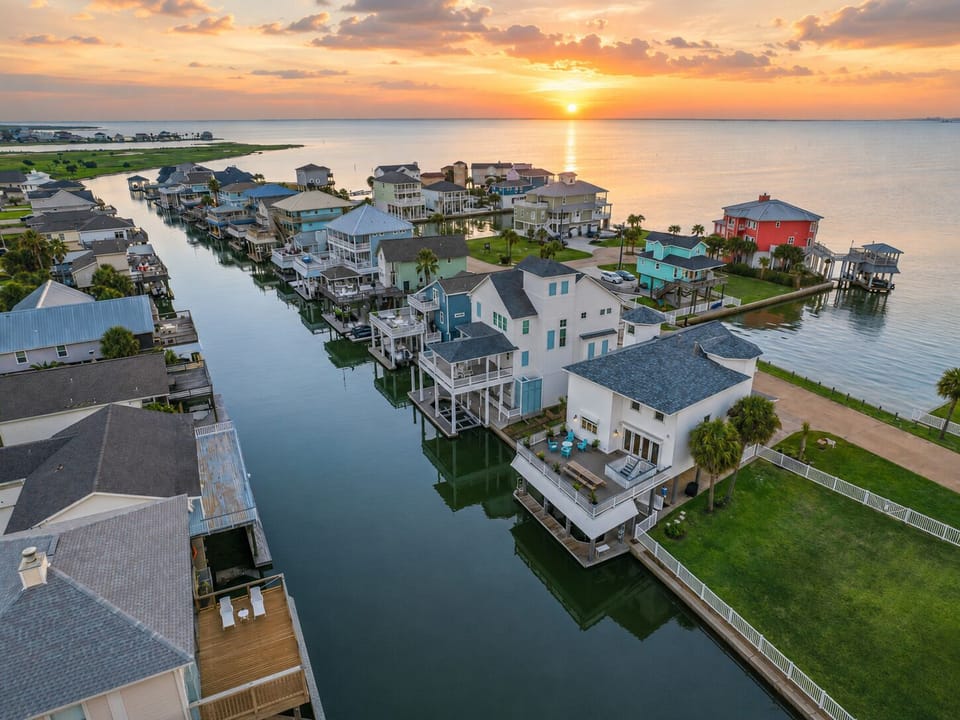 Aerial view of canal-front Galveston vacation home at Chiquita Street with private dock, fenced lawn, deck seating, and waterfront views.