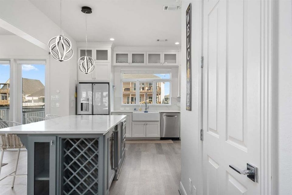 Modern kitchen view with white cabinetry, island seating, stainless refrigerator, wine rack, and open layout for group stays.