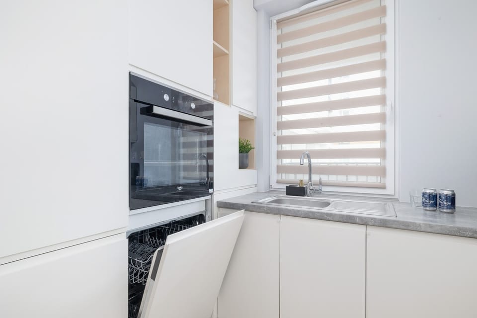 A modern kitchen with white cabinetry, a built-in oven, and a large window providing natural light.

