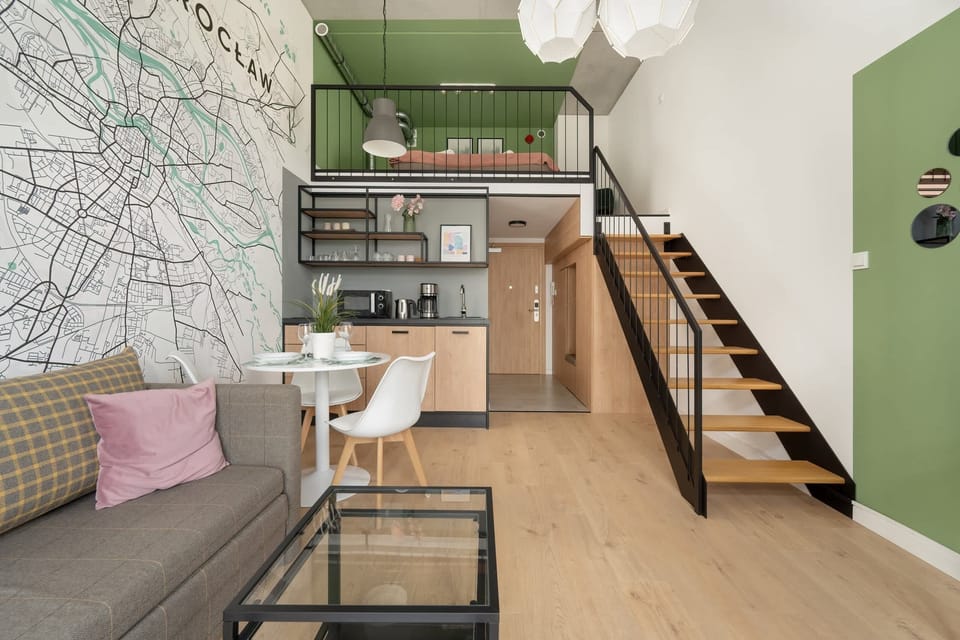 A view of the open-plan living space with a stairs leading to a mezzanine, complemented by a well-equipped kitchenette.

