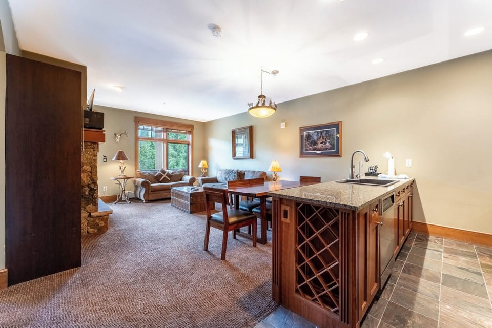 Unwind in your spacious open-concept living area with rich wood finishes, granite counters, and a cozy stone fireplace creating the perfect mountain retreat ambiance.