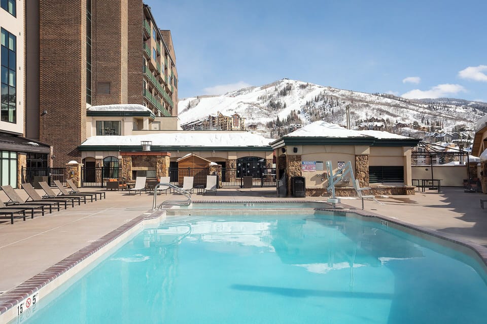 A beautiful mountain resort pool area surrounded by snow-capped peaks and modern accommodations.
