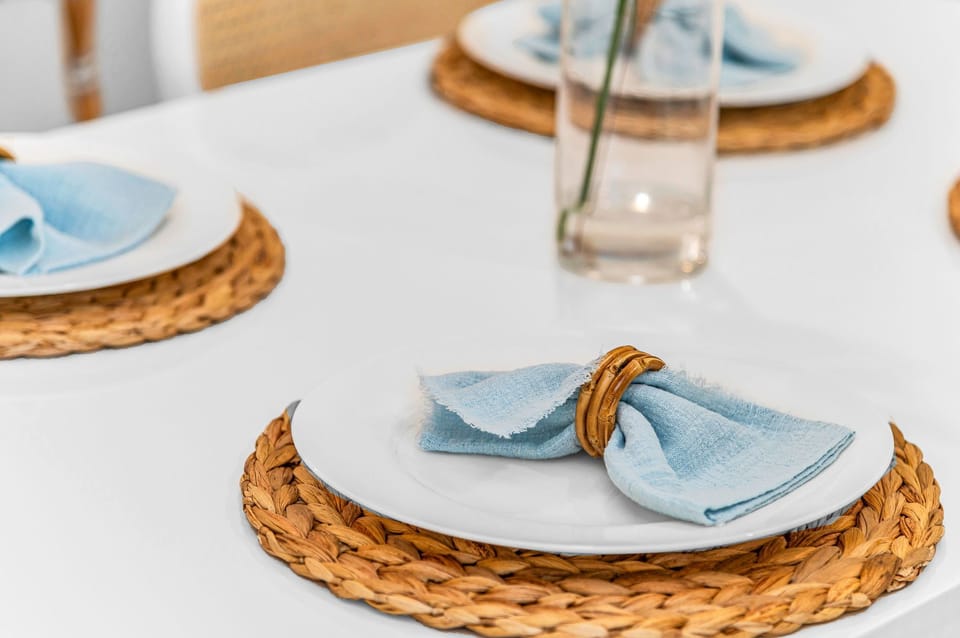 The modern white table seats 4 for intimate dining, There are 4 natural cane dining chairs to add to that coastal flair and an impressively large round rattan "sun" mirror that centers over the dining table.