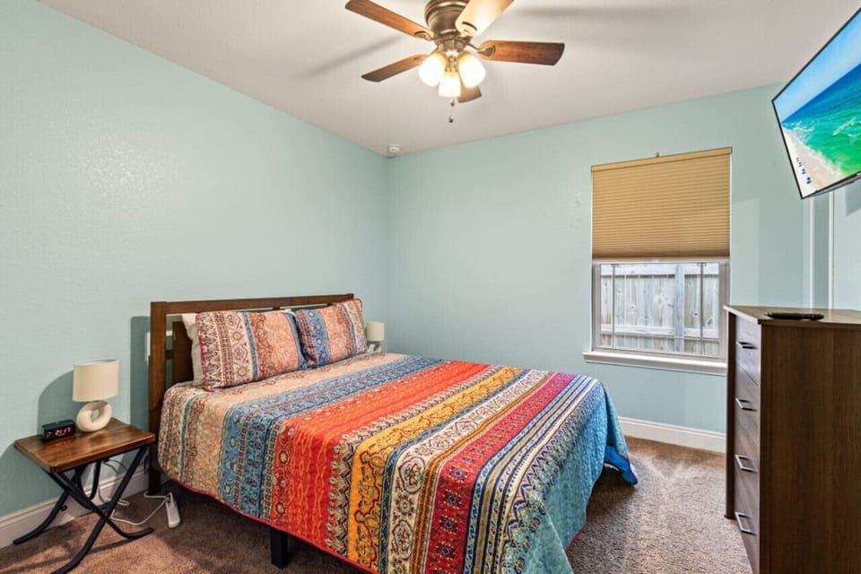 Unwind in the warm and inviting third bedroom, complete with a queen bed, a large flat-screen TV, a substantial dresser, a ceiling fan, and an alarm clock.