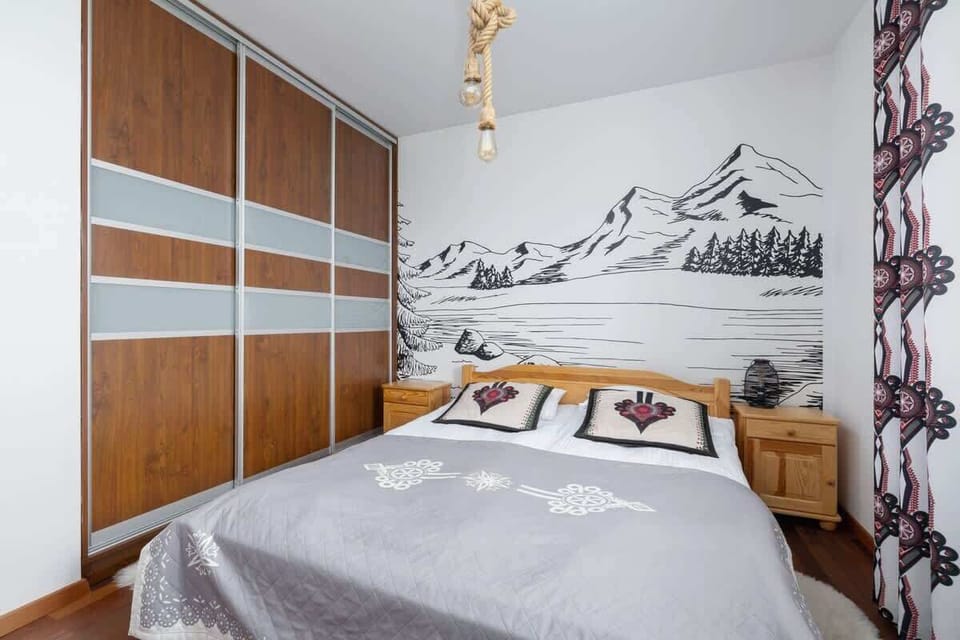 A bright bedroom with a double bed, wooden accents, and a mountain-inspired mural.

