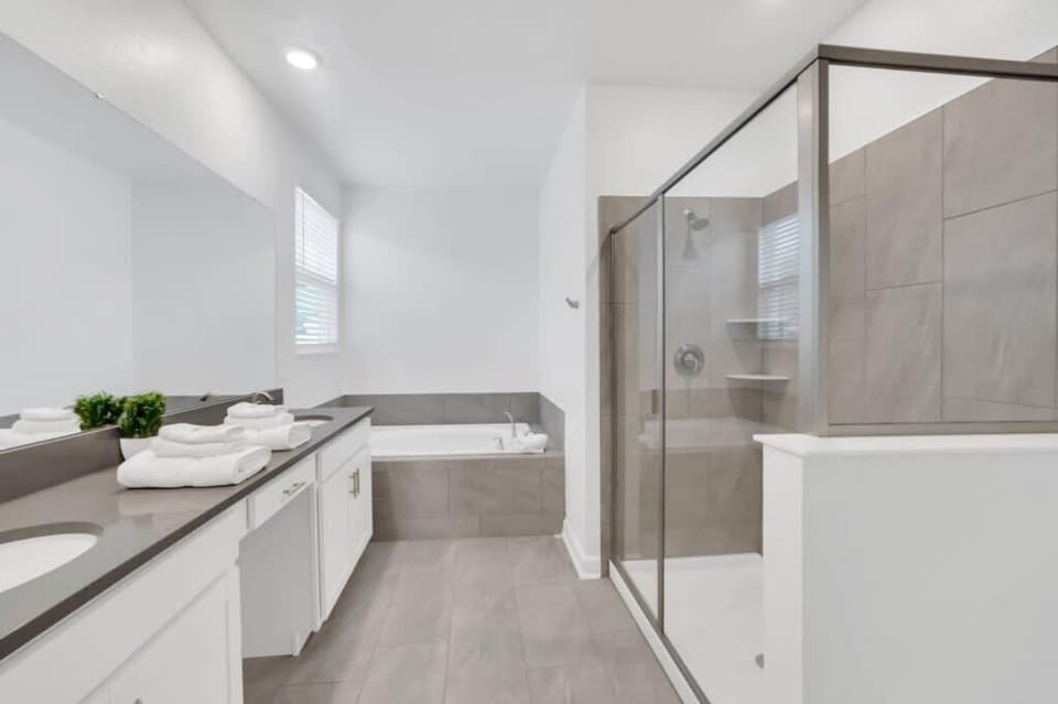 Spacious master bathroom featuring a double-sink vanity, separate tub, shower, bright lighting, and plenty of room to get ready comfortably.
