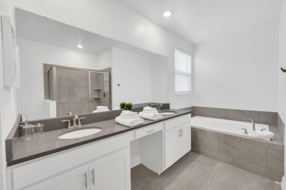 Spacious master bathroom featuring a double-sink vanity, separate tub, shower, bright lighting, and plenty of room to get ready comfortably.