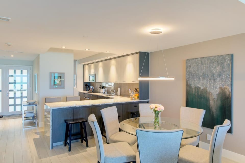 Light wood flooring and soft gray walls create a bright dining area with a round glass table and cushioned chairs.