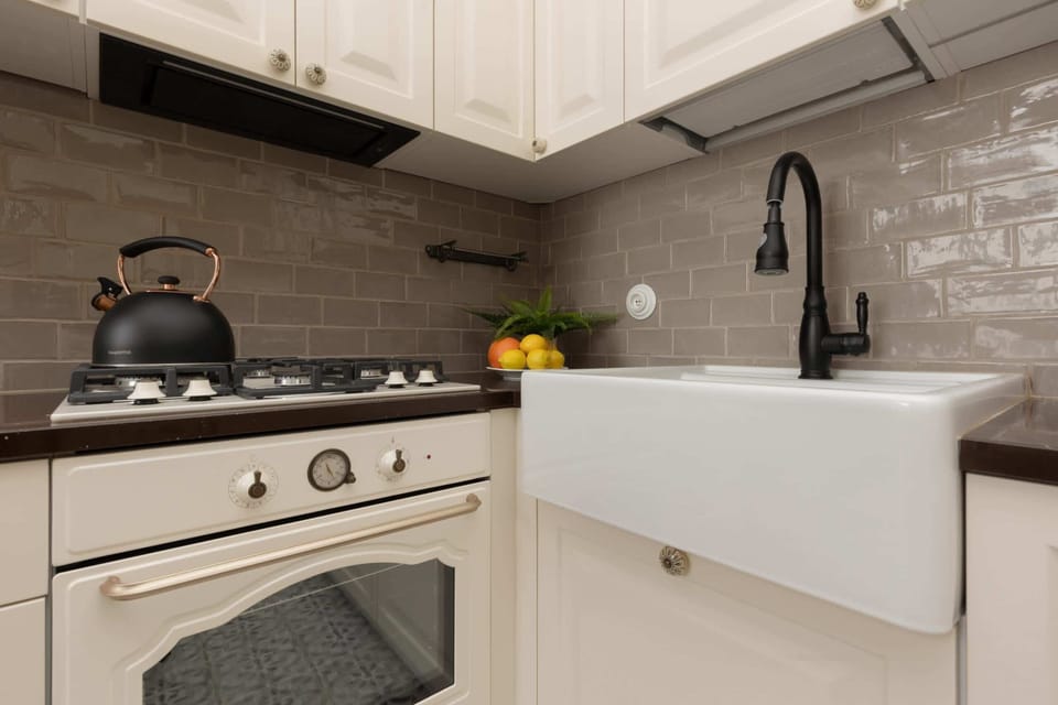 A functional kitchen corner with a stove, kettle, and elegant gray backsplash tiles.

