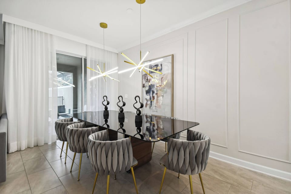 Join us at the sleek black dining table, where plush chairs add sophistication and a unique light fixture above creates a warm ambiance, perfect for enjoying meals and great conversations together.