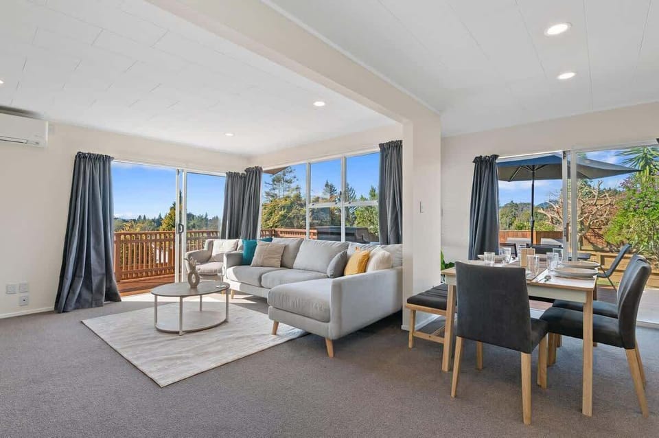 Spacious living and dining area with floor-to-ceiling windows and lush outdoor views — self-contained Rotorua accommodation
