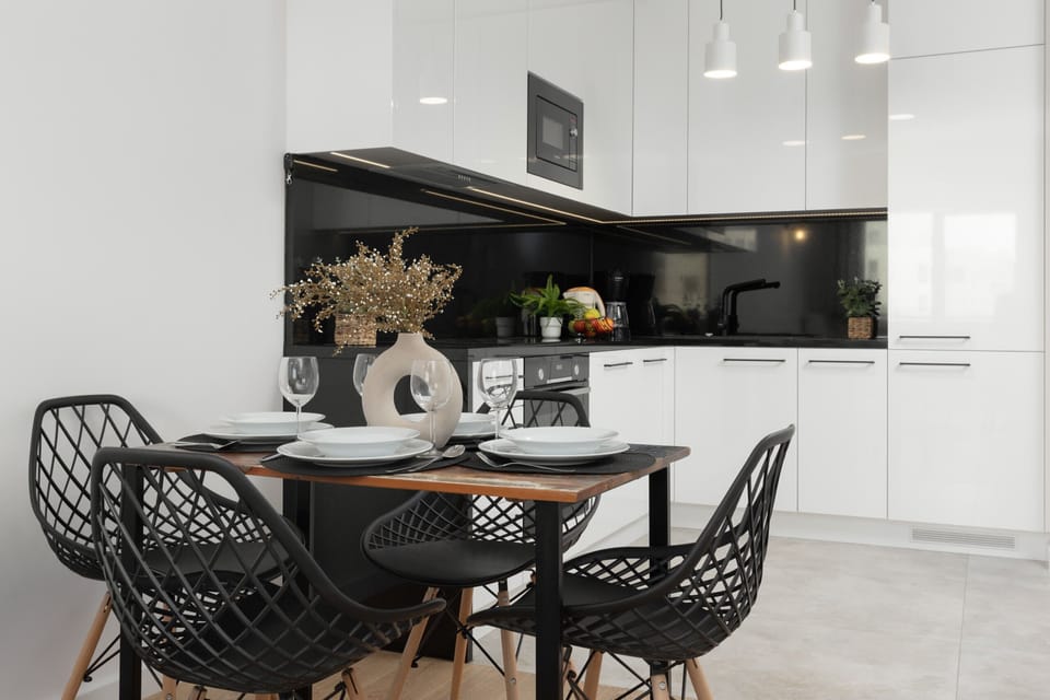 A sleek kitchen with black and white finishes and a round dining table for four.

