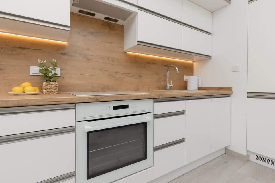 A contemporary kitchen with white cabinets, wooden countertops, and built-in appliances.

