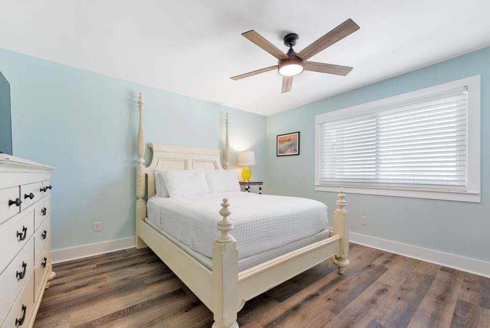 Drift off peacefully in your serene bedroom featuring soft blue walls, crisp linens, and a gentle ceiling fan for ultimate comfort.