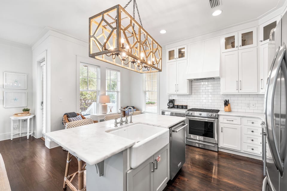 Bright chef’s kitchen with a farmhouse sink, marble island, stainless steel appliances, and elegant coastal-inspired finishes.