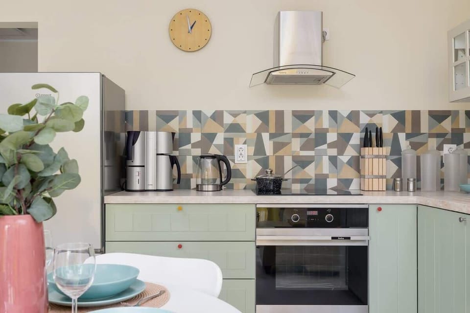 A modern kitchen with pastel green cabinets, patterned backsplash, and sleek appliances.

