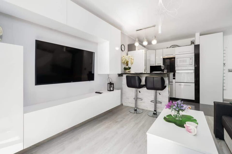 A bright and stylish living area with a mounted TV, minimalist decor, and an open-plan layout connecting to the kitchen.


