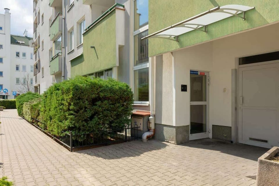 An exterior view of the building, showcasing a clean, paved walkway and a green hedge for added privacy.

