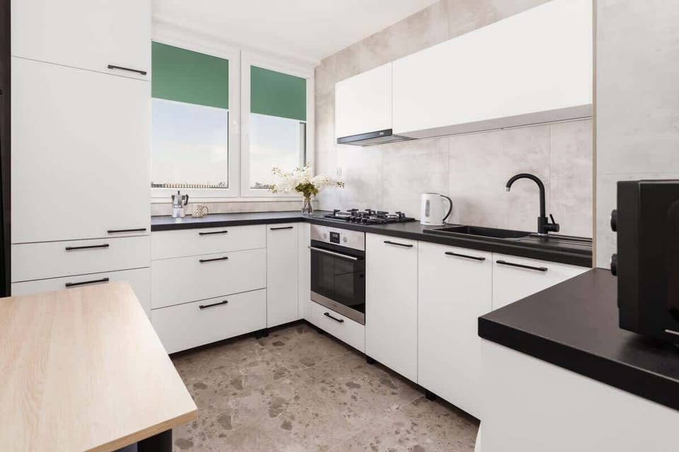 A modern kitchen layout with white cabinets, black countertops, and plenty of natural light.

