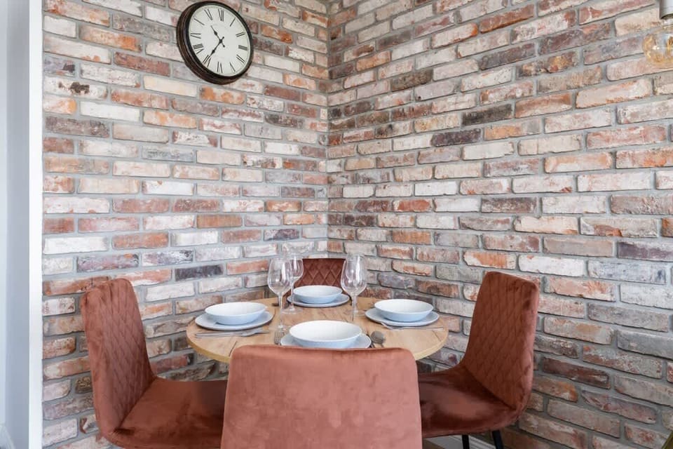 A stylish dining area with a brick backdrop, a small table, and comfortable upholstered chairs.

