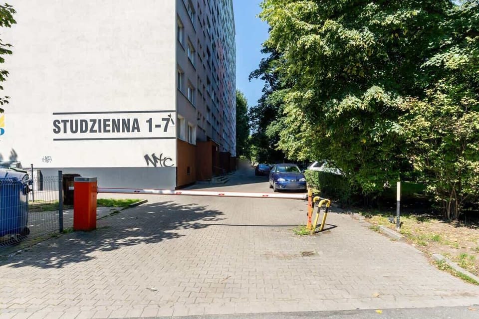 A street-level view featuring the entrance to a building marked "Studzienna 1-7," with trees and a clear sky in the background.






