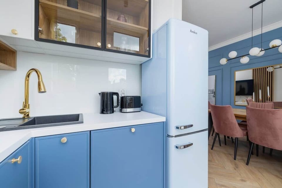 A compact kitchen setup with blue cabinets, a gold faucet, and modern appliances, including a coffee machine.

