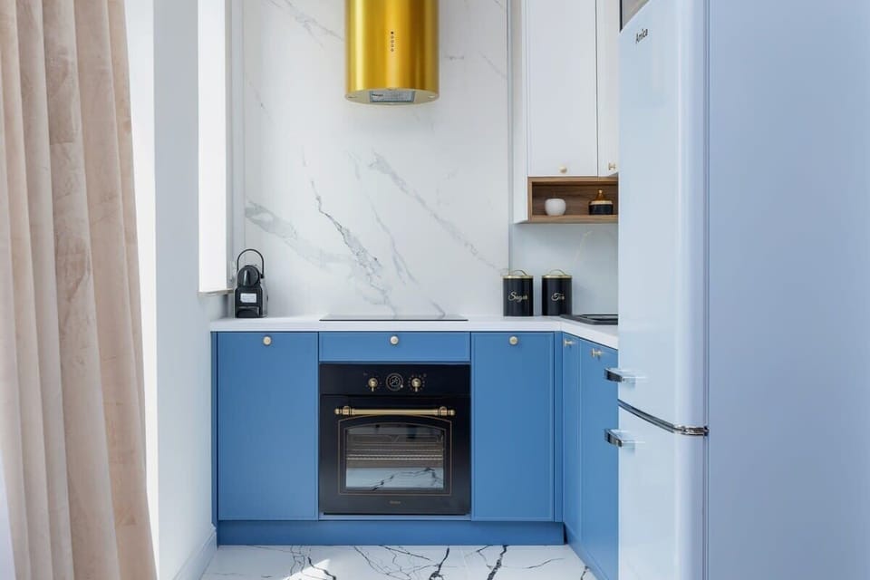A compact kitchen with blue cabinets, marble backsplash, and gold accents, blending functionality with luxury.

