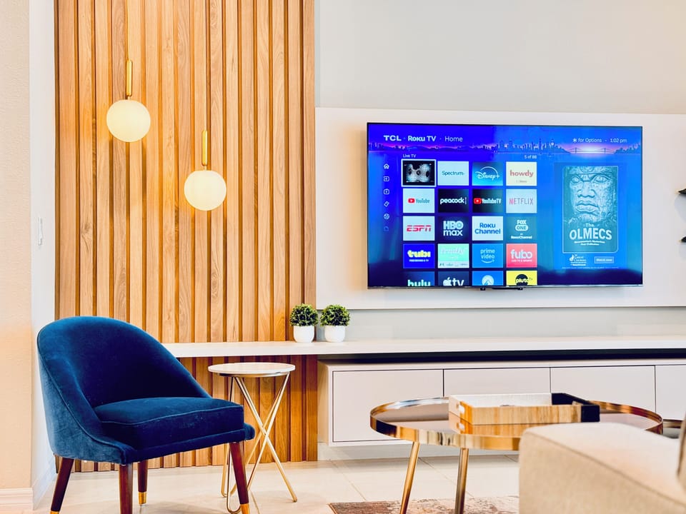 Living room detail with pendant lighting, TV, and blue velvet chair.