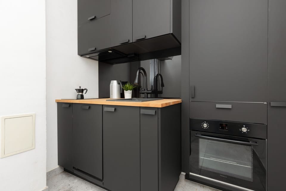 A compact, modern kitchen with dark cabinets, wooden countertops, and essential appliances.

