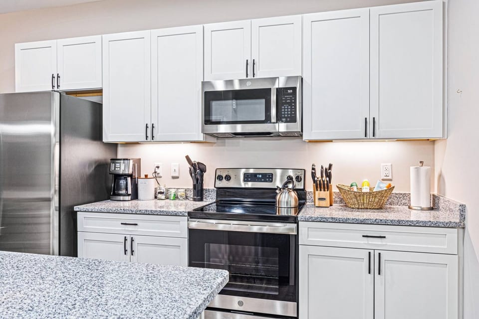 Step into our pristine, brand-new white kitchen featuring stainless steel appliances and a spacious island that seamlessly opens to the dining and living areas—ideal for your gatherings. ✨ #ModernLiving #HomeAwayFromHome