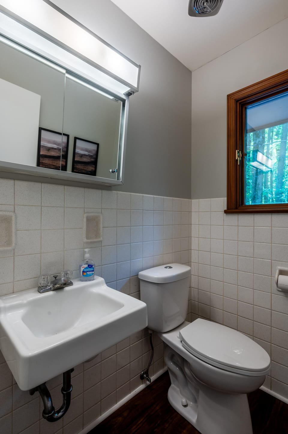 Bathroom features white square tile halfway up walls, a wall-mounted sink, and a wood-trimmed window.