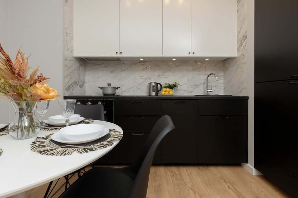 A refined kitchen design with black lower cabinets, white upper cabinets, and a marble-style backsplash.


