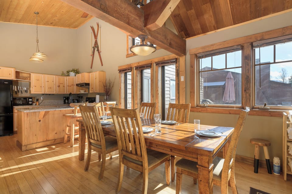 Gather around this rustic dining table where warm wood and natural light create your perfect mountain retreat atmosphere.