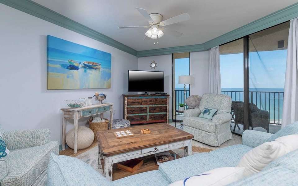 Bright living area featuring a rustic coffee table, cozy seating, and a TV, with expansive views of the beachfront beyond
