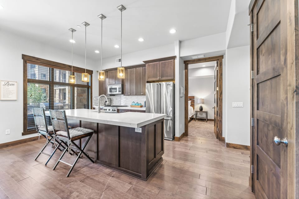 - Modern kitchen with stainless steel fridge and microwave included  
- Quartz countertops and pendant lights highlight the central island  
- Bar seating for two makes meals and casual chats convenient