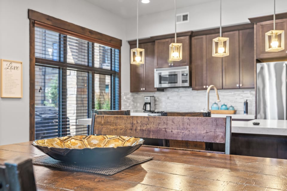 - Rustic dining table centerpiece adds charm to the kitchen setting  
- Pendant lighting illuminates stainless steel appliances and modern backsplash  
- Large windows bring natural light into the open dining and cooking space