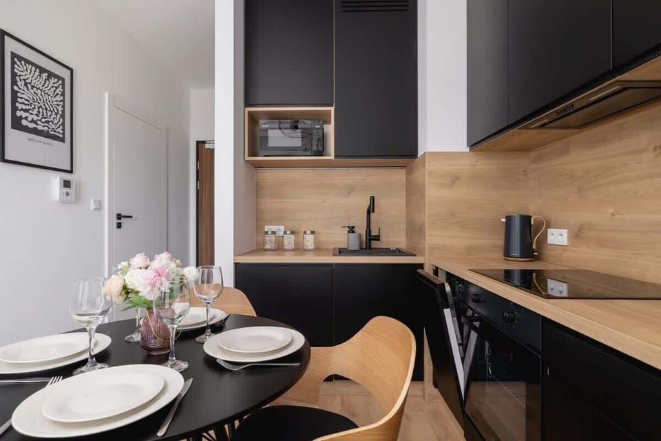 A closer angle of the dining space set for four, highlighting the sleek black kitchen cabinets and wooden countertops.
