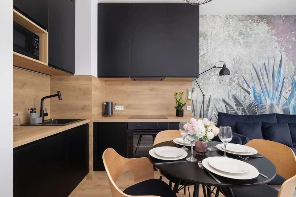 The open-concept kitchen area with black cabinetry, a warm wooden backsplash, and vibrant wall art as a stylish focal point.
