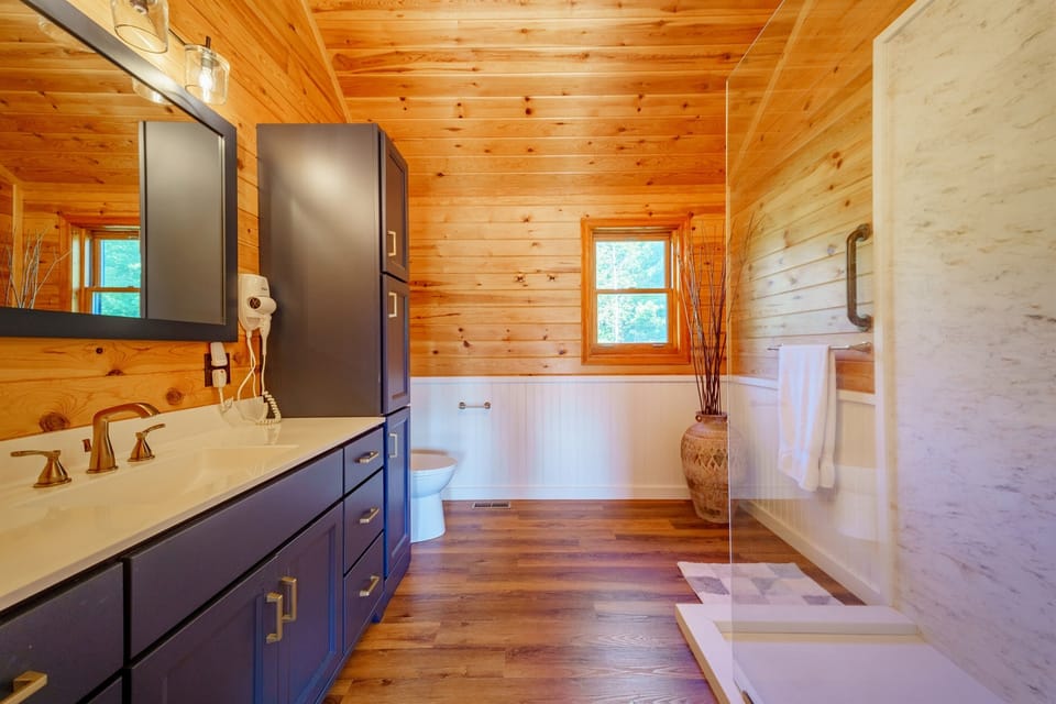 Enjoy a spa-like experience in our luxurious master ensuite bathroom featuring a European shower with a rain shower  head, custom cabinetry, and knotty pine paneling